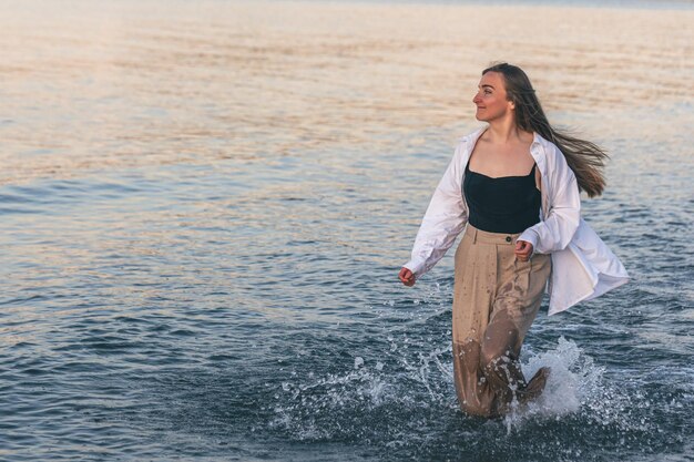 Una mujer camina descalza por el mar en el espacio de la copia al atardecer