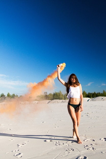 Mujer camina con humo en la playa blanca bajo el cielo azul