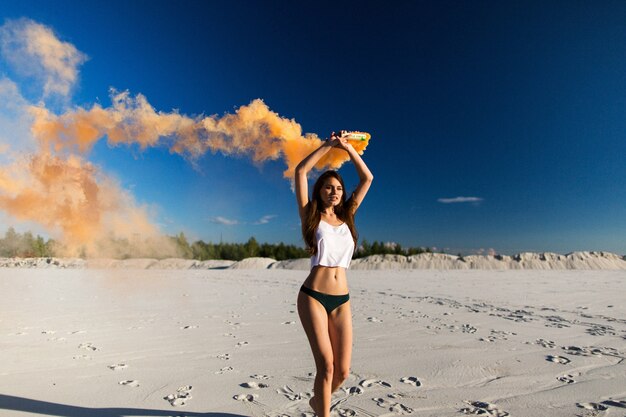Mujer camina con humo en la playa blanca bajo el cielo azul