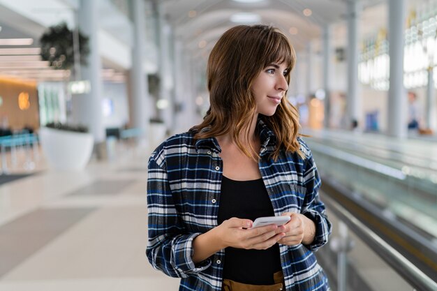 Mujer caminando por el aeropuerto con su dispositivo de teléfono inteligente.