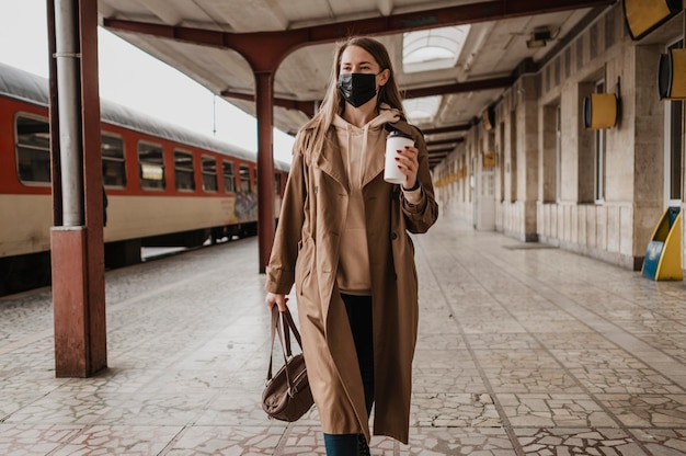 Mujer caminando con un café en una estación de tren