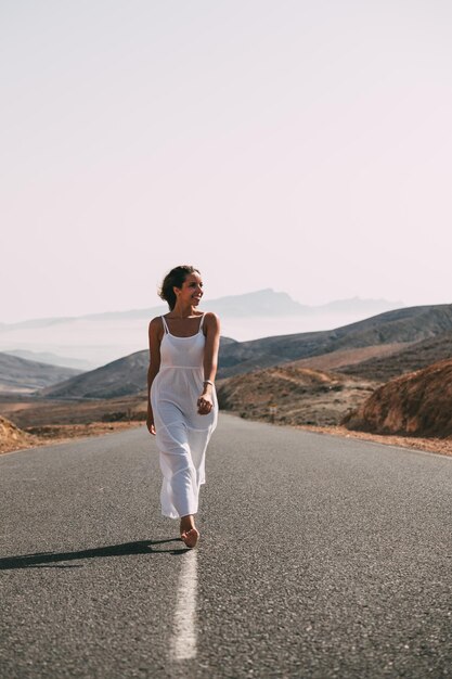 Mujer caminando por la carretera cerca de las colinas bajo el cielo nublado