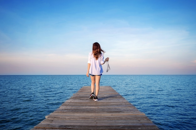 Mujer caminando sobre un puente de madera extendido hacia el mar.