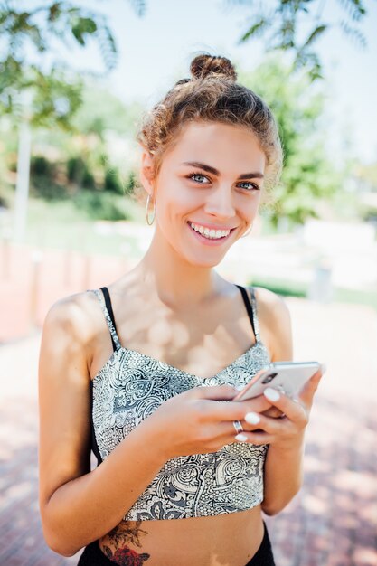 Mujer caminando y usando un teléfono inteligente en la calle en un día soleado de verano