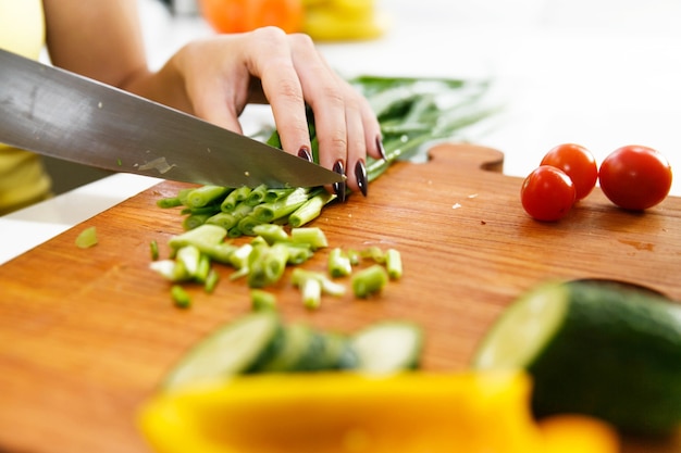 La mujer en camisa amarilla corta la cebolla verde en la cocina