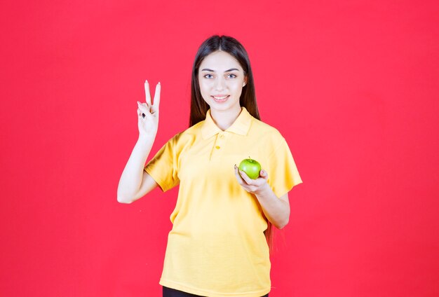 mujer con camisa amarilla sosteniendo una manzana verde y sintiéndose satisfecha.