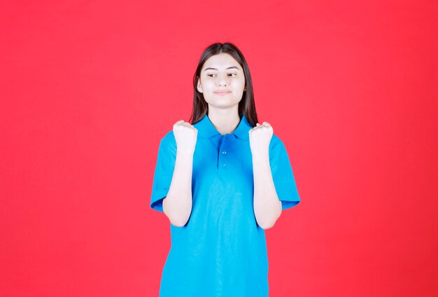 mujer en camisa azul de pie y mostrando un signo de mano positivo.