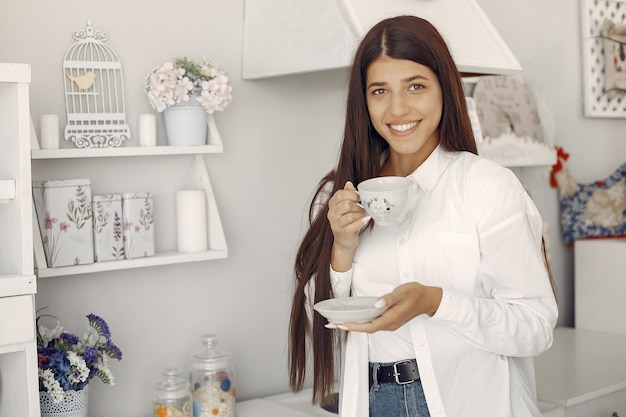 Mujer en una camisa blanca de pie en la cocina y tomando un café