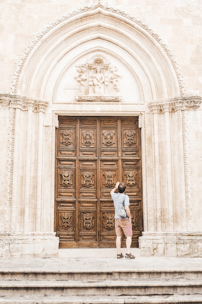 Mujer con camisa blanca de pie delante de la puerta de madera marrón