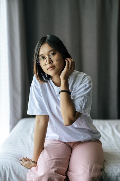 Una mujer con una camisa blanca sentada en la cama y mirando.