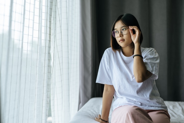 Una mujer con una camisa blanca sentada en la cama y mirando.