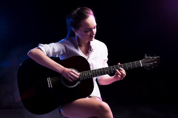 Mujer en camisa blanca tocando la guitarra en el escenario