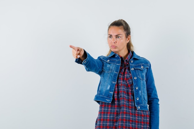 Mujer en camisa, chaqueta apuntando hacia afuera y mirando enfocado, vista frontal.