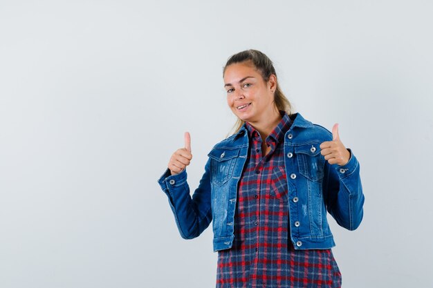 Mujer en camisa, chaqueta mostrando doble pulgar hacia arriba y mirando alegre, vista frontal.