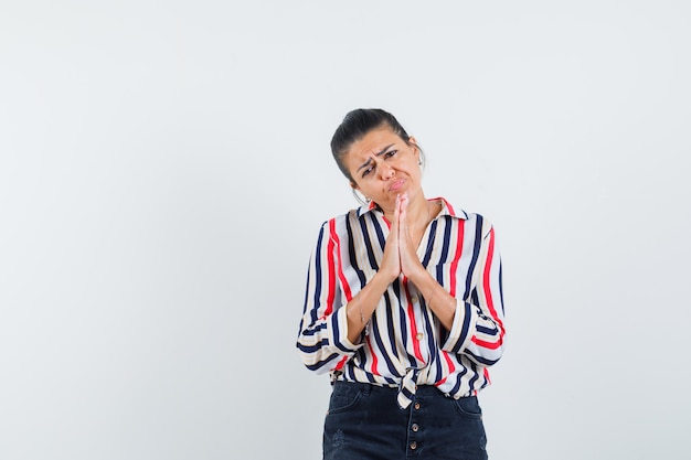 Foto gratuita mujer en camisa, falda mostrando gesto de namaste y mirando humilde