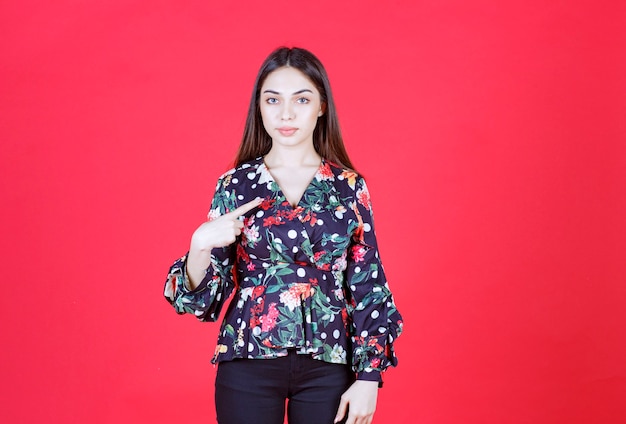 mujer en camisa floral de pie sobre la pared roja y presentándose.