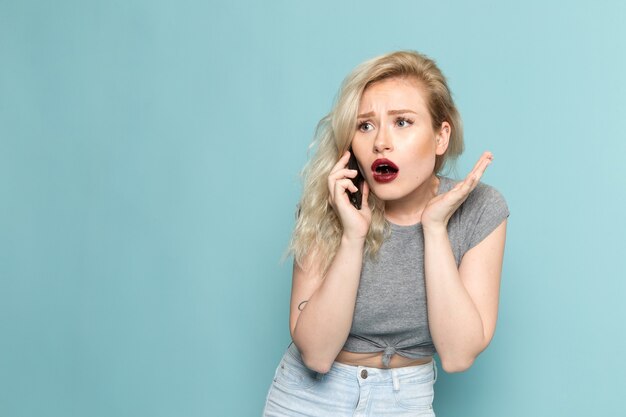 mujer en camisa gris y jeans azul brillante hablando por teléfono