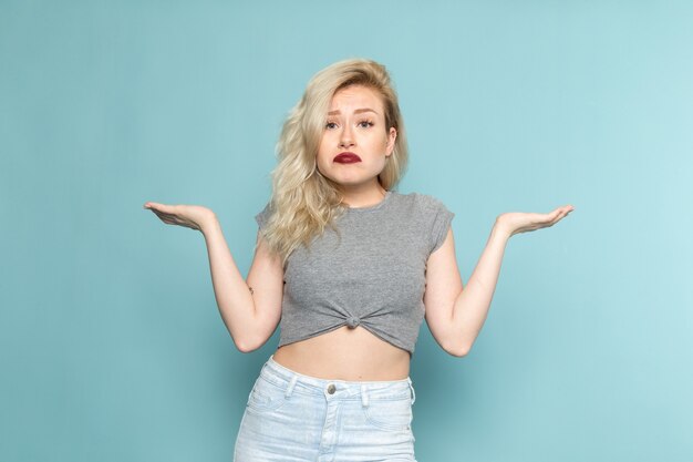 Mujer en camisa gris y jeans azul brillante posando con expresión desconocida