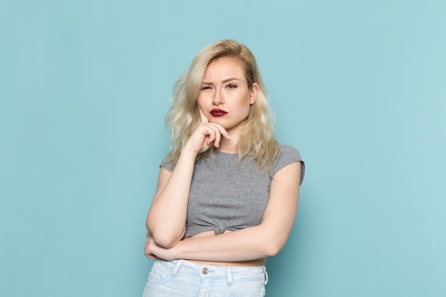 Mujer en camisa gris y jeans azul brillante posando con expresión de pensamiento