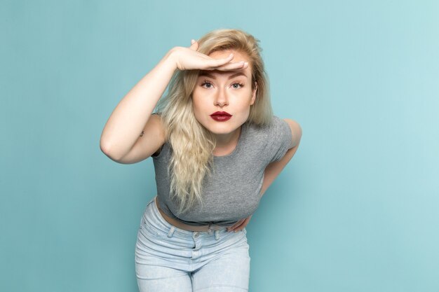 Mujer en camisa gris y jeans azul brillante posando y mirando en la distancia