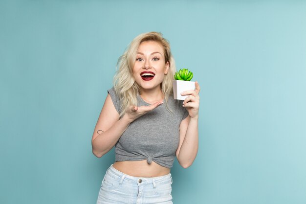 mujer con camisa gris y jeans azul brillante sosteniendo una pequeña planta