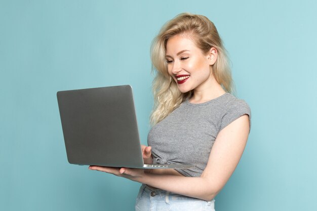 Mujer en camisa gris y jeans azul brillante usando laptop