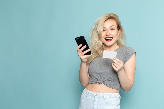 Mujer en camisa gris y jeans azul brillante usando un teléfono con expresión feliz