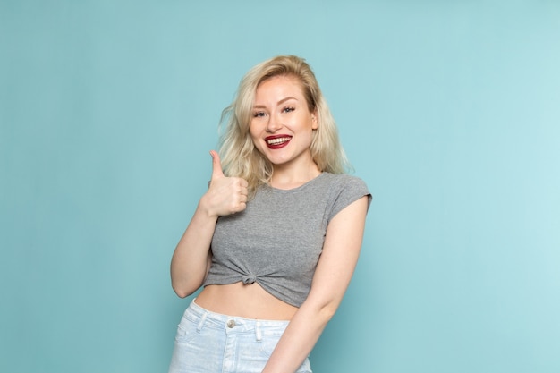 mujer en camisa gris y pantalones vaqueros azules brillantes posando con expresión encantada