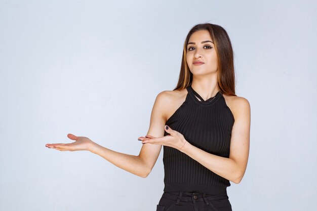 Mujer en camisa negra abriendo la mano y sosteniendo o presentando algo.