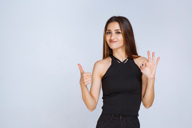 Mujer en camisa negra haciendo signo de mano positivo.