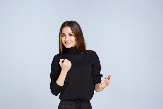 mujer con camisa negra mostrando su puño y se ve poderosa.