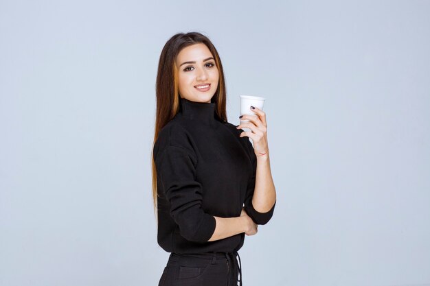 mujer en camisa negra sosteniendo una taza de café desechable y promocionándola.