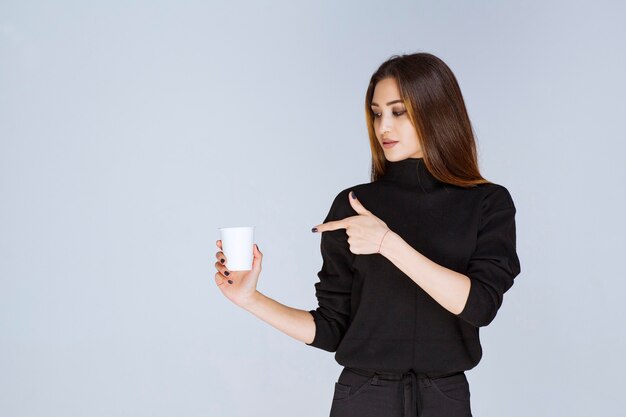 mujer en camisa negra sosteniendo una taza de café desechable y promocionándola.