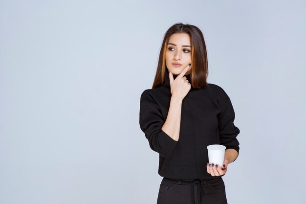 mujer en camisa negra sosteniendo una taza de café y pensando en nuevas ideas.