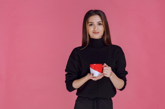 Mujer en camisa negra sosteniendo una taza de café y sonriendo.