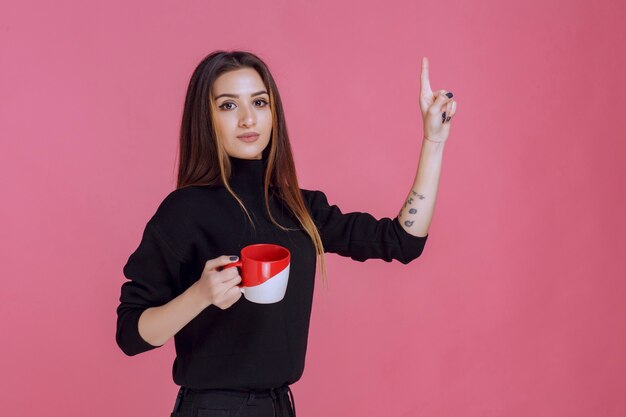 Mujer en camisa negra sosteniendo una taza de café y sonriendo.