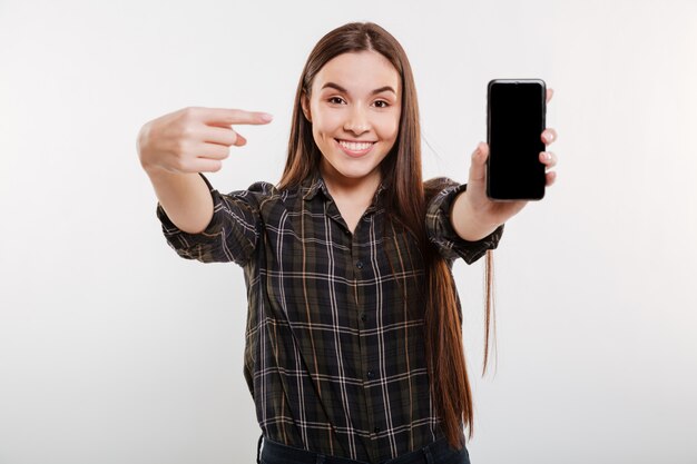 Mujer en camisa que muestra la pantalla del teléfono inteligente en blanco
