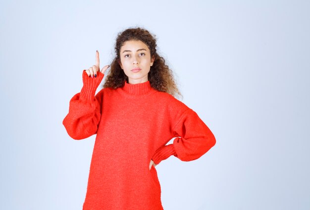 mujer con camisa roja apuntando a alguien o en algún lugar con cara emocional en azul.