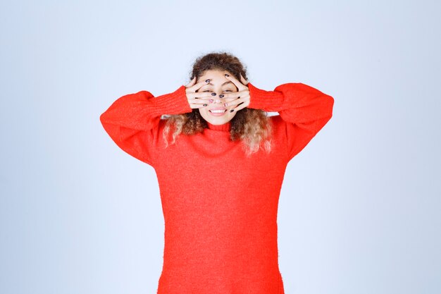 mujer con camisa roja mirando a través de sus dedos y riendo.