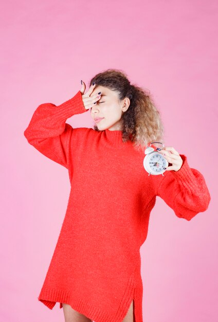 mujer de camisa roja con reloj despertador y parece somnolienta.