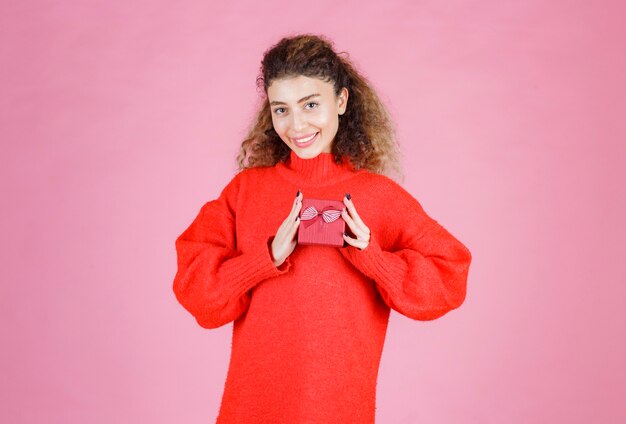 mujer en camisa roja sosteniendo una pequeña caja de regalo roja.