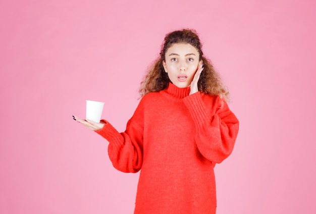 mujer de camisa roja sosteniendo un vaso desechable y pensando.