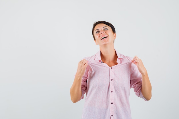 Mujer en camisa rosa tirando de su camisa y mirando orgullosa, vista frontal.