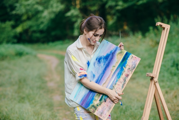 Mujer con la camiseta manchada de pintura mirando un cuadro que está en su mano