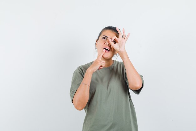 Mujer en camiseta mostrando signo ok en el ojo y mirando pensativo