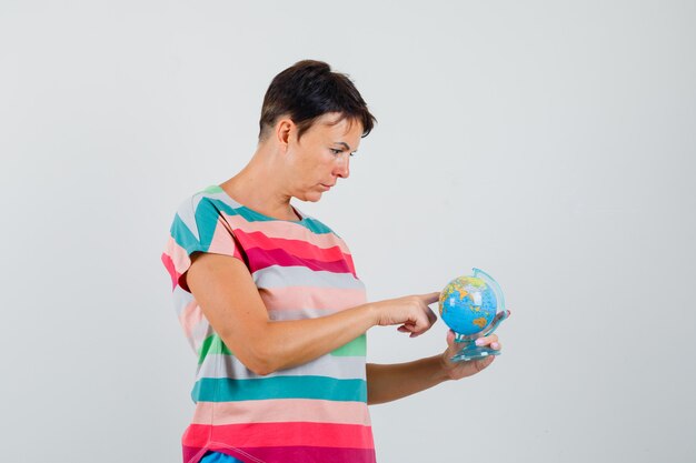 Mujer en camiseta a rayas eligiendo destino en modelo de globo y mirando enfocado