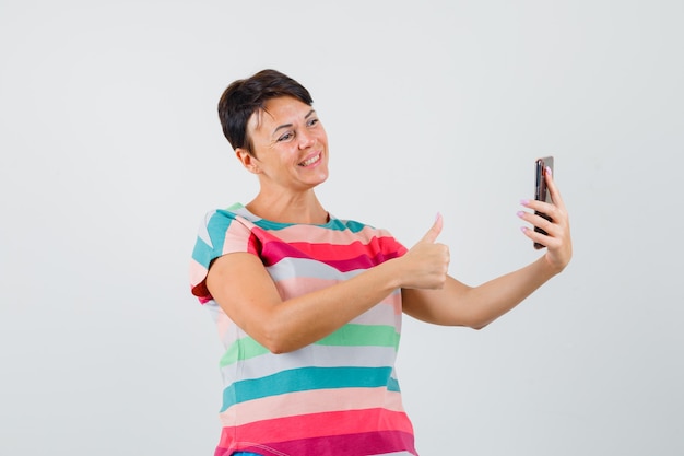 Mujer en camiseta a rayas mostrando el pulgar hacia arriba en el chat de video y mirando alegre, vista frontal.