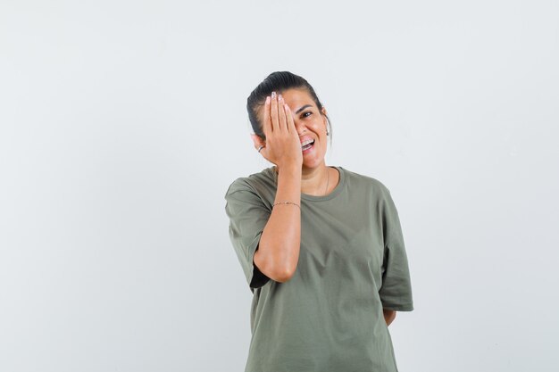 mujer en camiseta sosteniendo la mano en el ojo y mirando feliz