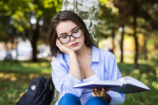 Mujer cansada en gafas estudia contra el parque verde de verano.