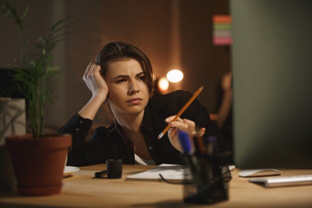 Mujer cansada con lápiz trabajando con computadora